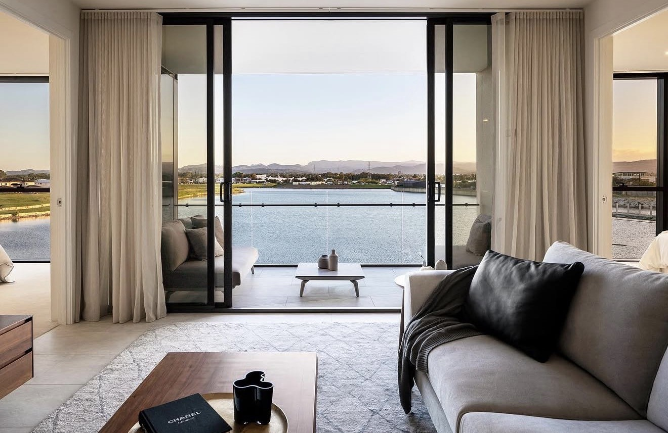 Luxury waterside apartment interior with floor-to-ceiling glass opening to a balcony over calm water